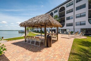 A patio area with a thatched umbrella, lounge chairs, and a view of the water. - Waterfront 3BR/2BA condo with pool, marina access, WiFi, and heated pool. (Marco Island)