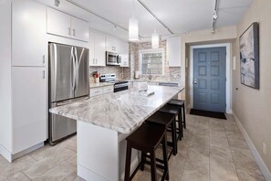 A modern kitchen with white cabinetry, stainless steel appliances, a marble countertop, and a blue door.