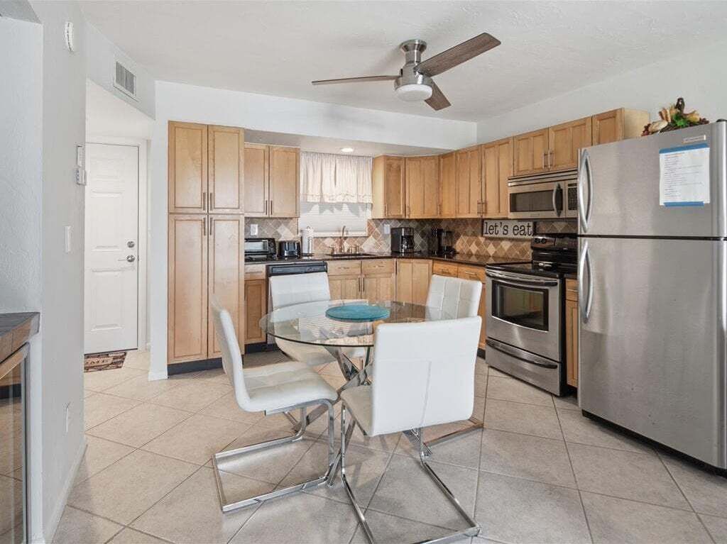 A modern kitchen with wooden cabinets, a stainless steel refrigerator, a microwave, and a dining table with white chairs.