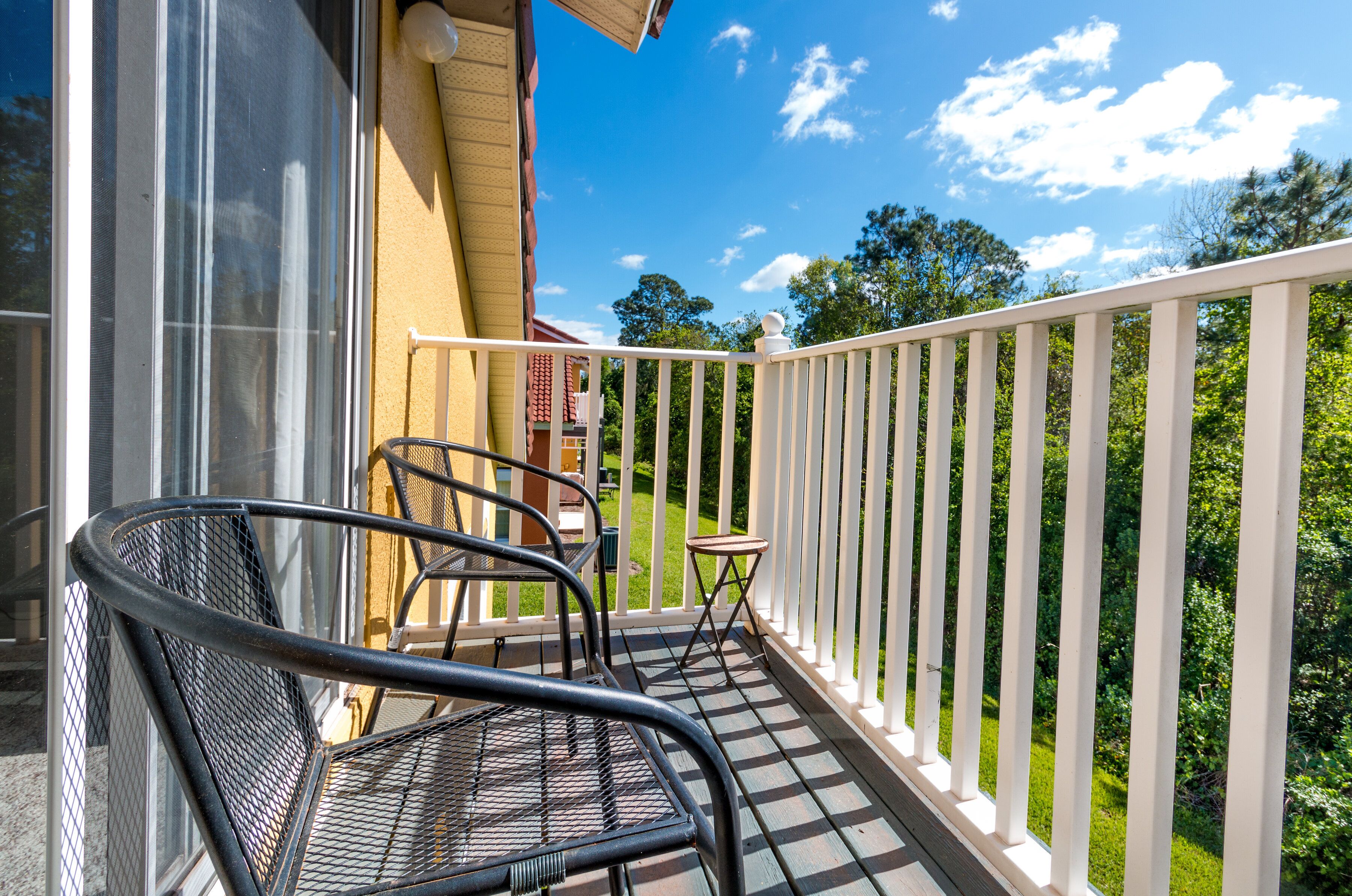 A balcony with a metal chair and a small table, overlooking a green landscape.