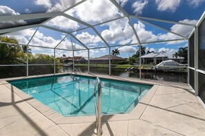A clear swimming pool with a metal roof structure, surrounded by a paved deck.