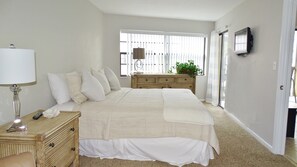 A bedroom with a large bed, a bedside table with a lamp, a dresser, and a window with blinds.