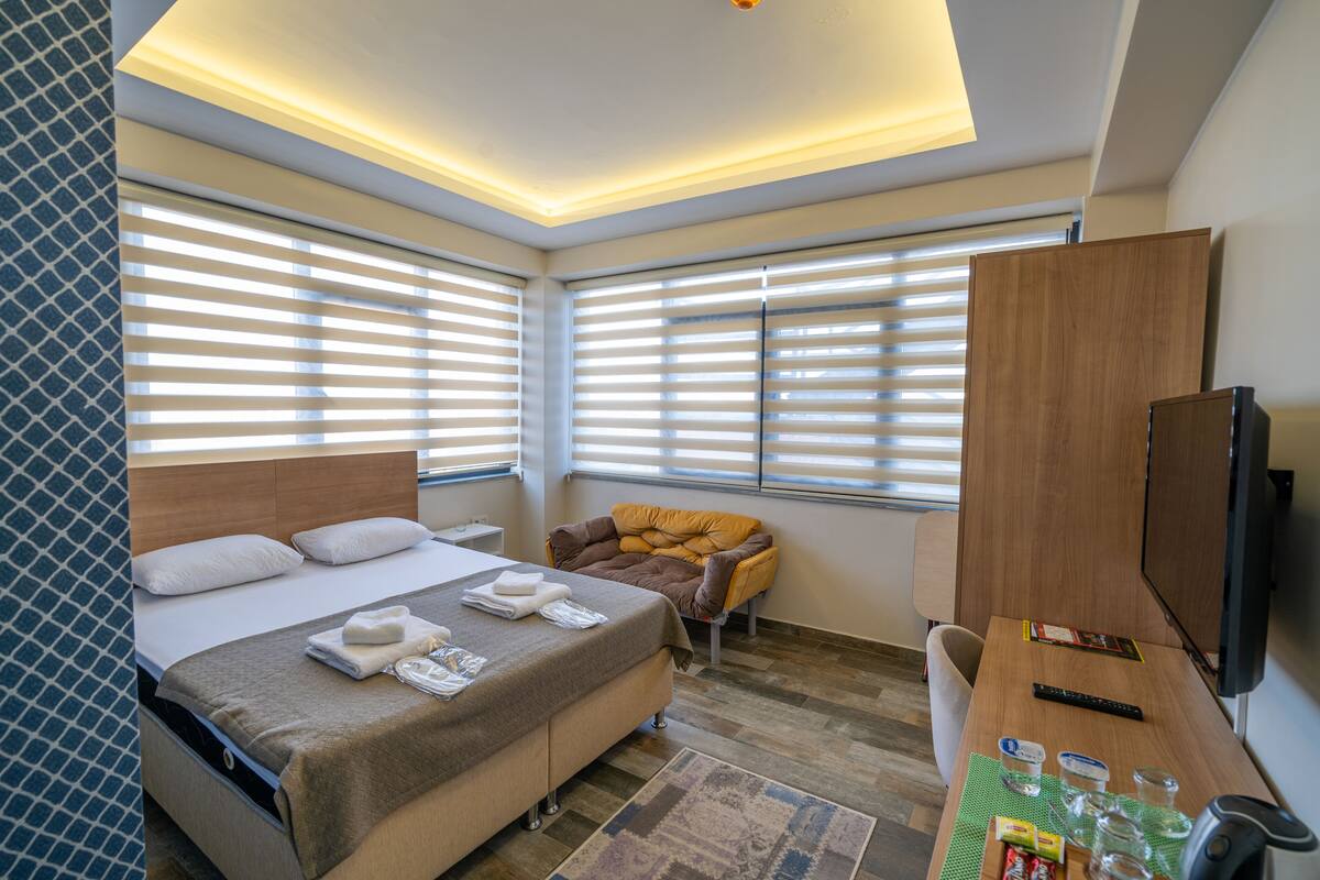 A hotel room with a bed, a seating area with a chair, a desk with a remote control, and a television.