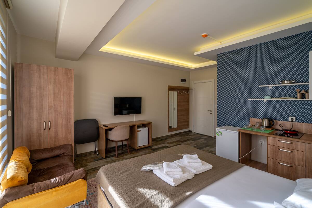 A modern hotel room with a bed, a desk, a television, and a kitchenette.