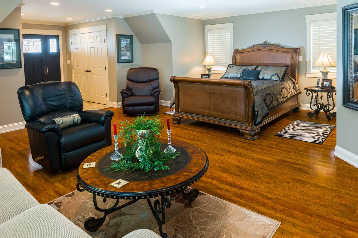 A bedroom with a large bed, two chairs, a round table with candles, and a door in the background.