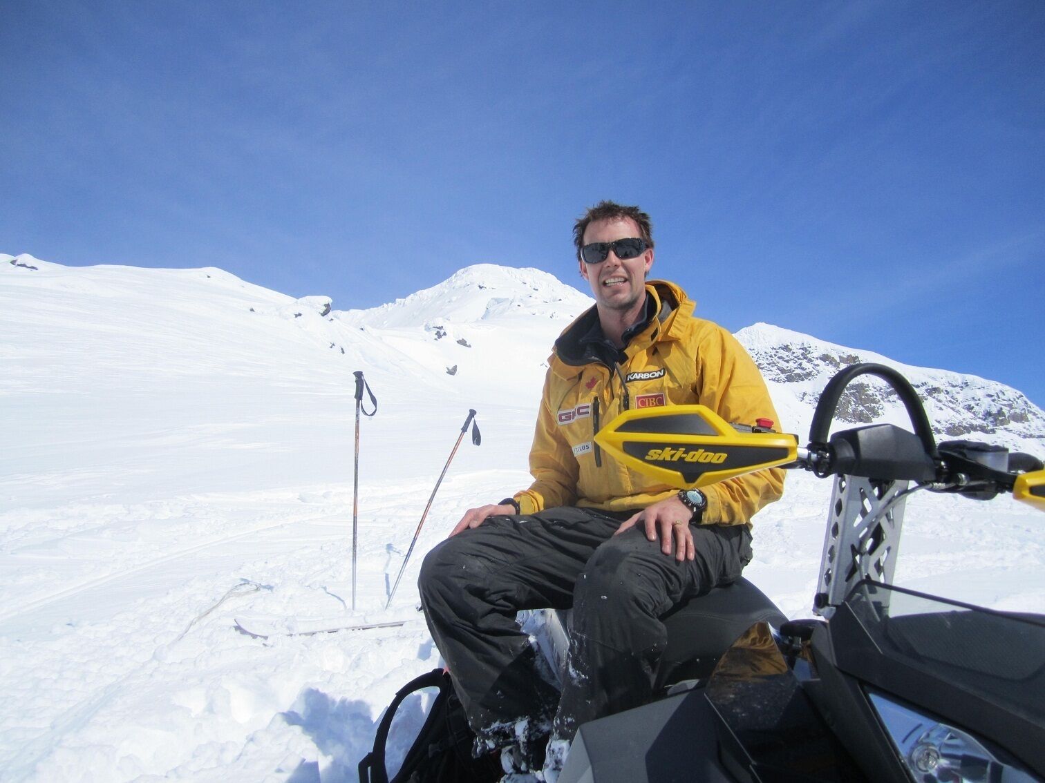 A person sitting on a ski-doo in a snowy environment with a clear sky.