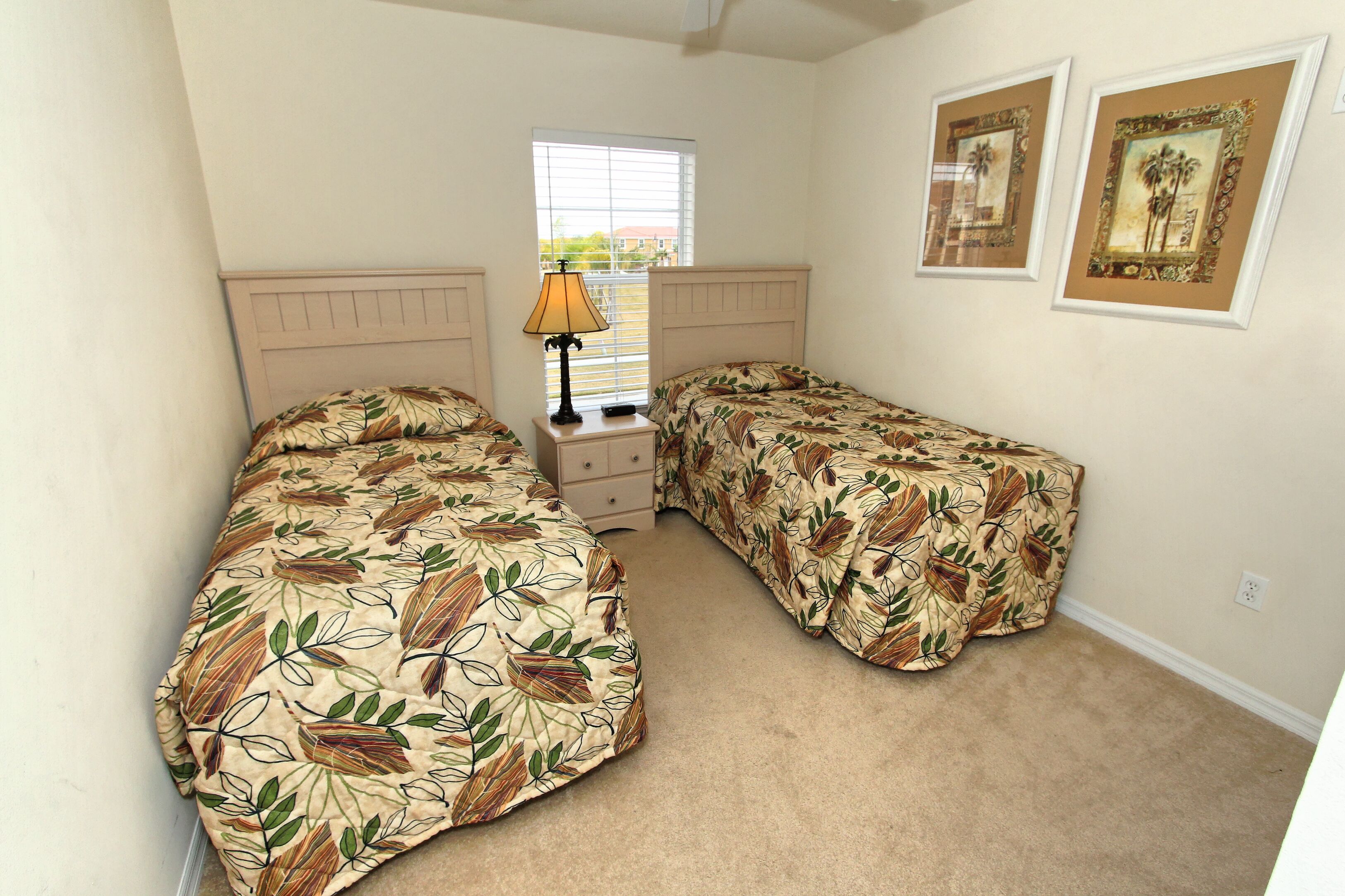A bedroom with two beds, a nightstand, a lamp, and two framed pictures on the wall.