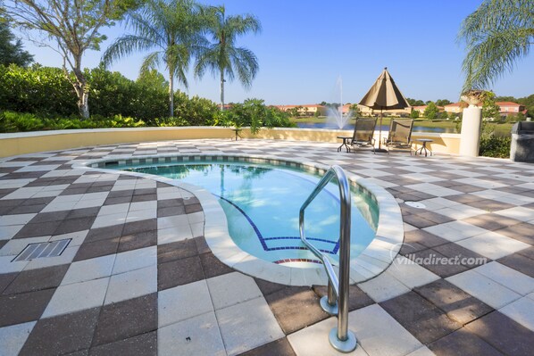 A pool with a checkered tile pattern, surrounded by lounge chairs and a view of a body of water and buildings in the distance. - Mickeys Lodge by VillaDirect (Kissimmee)