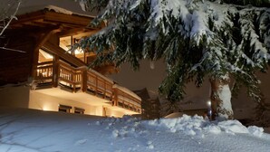 Een houten chalet met meerdere verdiepingen en balkons, omringd door sneeuwbedekte grond en bomen.