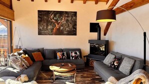 Een gezellige woonkamer met een hoog houten plafond, een open haard en een groot schilderij van een hert.