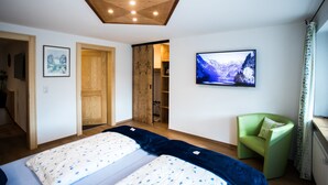 Un dormitorio con una cama, un televisor, una silla verde y techo de madera.