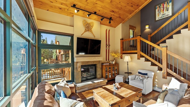 Ein geräumiges Wohnzimmer mit Kamin, großen Fenstern, einer Treppe und Wandbildern mit Ski-Motiven.