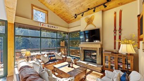 Ein gemütliches Wohnzimmer mit Kamin, großen Fenstern und Skiausrüstung an der Wand.