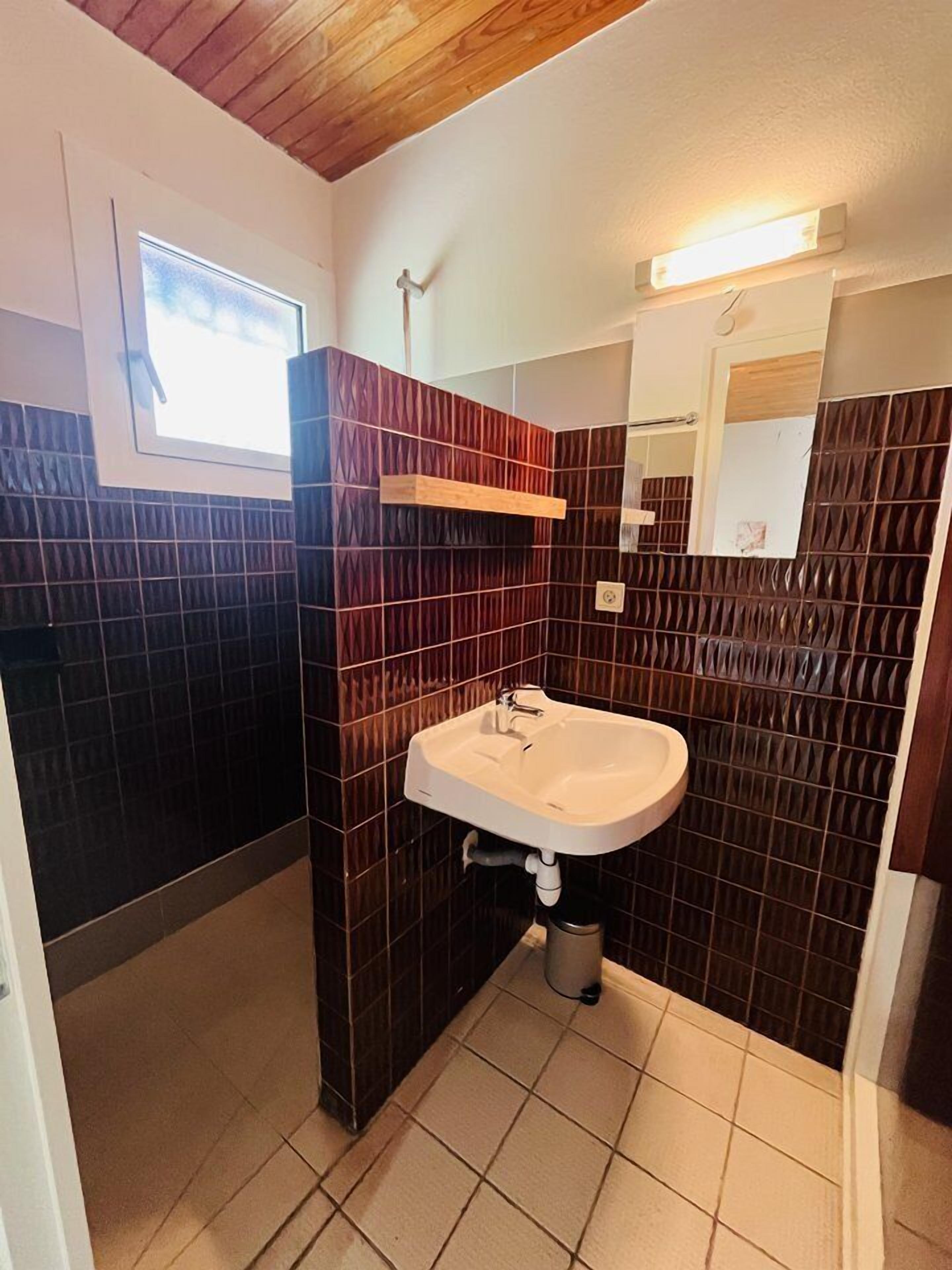 A bathroom with dark patterned tiles, a white sink, a window, and a mirror.