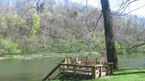 A wooden deck with chairs by a river, surrounded by trees. - Riverfront, pet friendly ! Log cabin with 2 bedrooms and loft! (Luray)