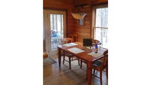 A wooden interior with a dining table, chairs, a hanging light fixture, and a view through the window. - Riverfront, pet friendly ! Log cabin with 2 bedrooms and loft! (Luray)