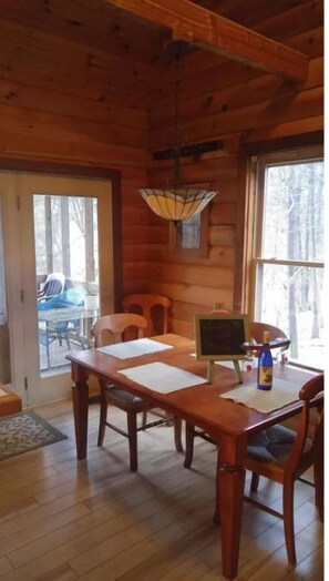 A wooden interior with a dining table, chairs, a hanging light fixture, and a view through the window. - Riverfront, pet friendly ! Log cabin with 2 bedrooms and loft! (Luray)