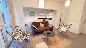 Een moderne woonkamer met een bruine bank, gestreepe fauteuils, een klein rond tafeltje en uitzicht op de keuken.