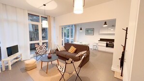 Een moderne woonkamer met een bank, salontafel en stoelen, een eethoek met tafel en stoelen, en een keuken met kasten en apparatuur.