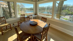 A dining room with a round table and six chairs, large windows with a view of a lake and trees, and decorative plates on the walls. - Luxury Home with Amazing Water Views - Perfect for an intimate family gathering (Mamaroneck)