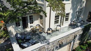 A patio area with outdoor seating, a stone wall, and a garage door. - Luxury Home with Amazing Water Views - Perfect for an intimate family gathering (Mamaroneck)