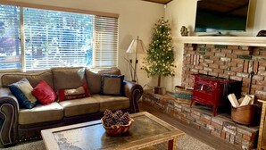 Een gezellige woonkamer met een leren bank, een houten salontafel, een open haard van baksteen en een kerstboom.