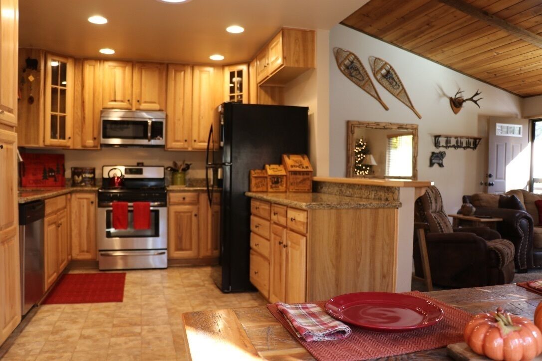 A kitchen with wooden cabinets, stainless steel appliances, and a dining area with a red table and chairs.