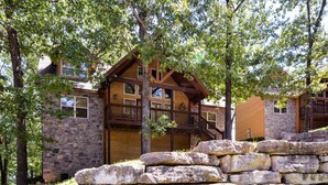 A stone building with a wooden balcony and a stone wall in front. - Close to SCD, Both Indoor & Outdoot pools, Possum Tracks Lodge  4BR/4BA Lodge (Branson West)