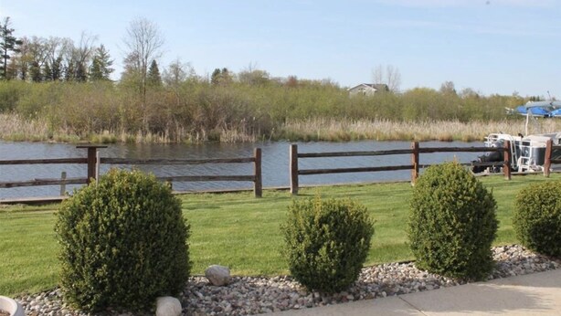 Une vue sur le lac, avec une clôture en bois, des arbustes taillés avec soin et un quai où sont amarrés des bateaux.