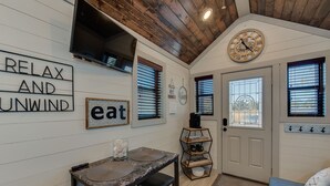 A cozy kitchen with a wooden ceiling, a dining table with stools, and a sign that reads "RELAX AND UNWIND." - Newly Built Tiny House Near College Station and Round Top Area (Caldwell)
