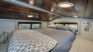 A bedroom with a large bed, wooden ceiling beams, and a window with blinds. - Newly Built Tiny House Near College Station and Round Top Area (Caldwell)