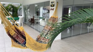 A modern interior with a hammock chair, a glass wall, and a dining area. - Beira Mar House in Angra dos Reis - Close to commerce in secure condominium (Angra dos Reis)