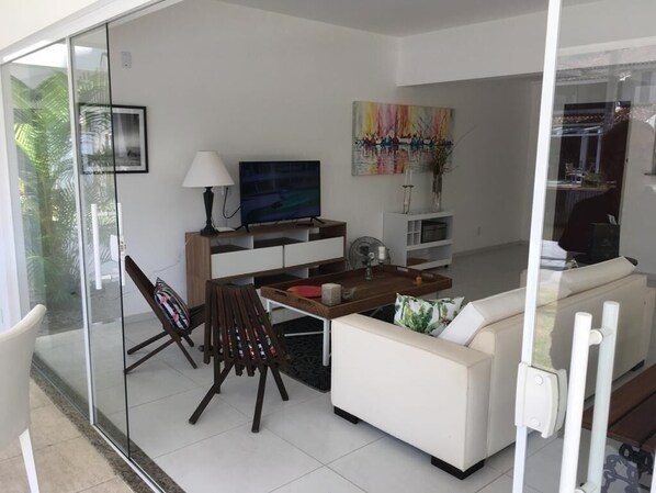 A modern living room with a glass partition, a sofa, a coffee table, a TV, and a painting on the wall. - Beira Mar House in Angra dos Reis - Close to commerce in secure condominium (Angra dos Reis)