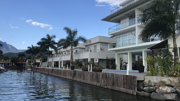 A waterfront hotel with a wooden dock, modern architecture, and palm trees. - Beira Mar House in Angra dos Reis - Close to commerce in secure condominium (Angra dos Reis)