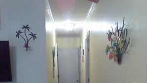 Un pasillo estrecho con piso de madera, paredes blancas y un techo con vigas a la vista. Se observan dos puertas a la derecha y un adorno en la pared izquierda.