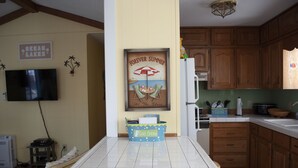 Una cocina con armarios de madera, salpicadero de azulejos, refrigerador y encimera con una cesta azul que dice 'Bebidas Frías'.