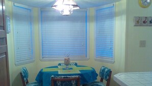 Un comedor con mantel azul, cuatro sillas, una barra de madera y un ventilador de techo.