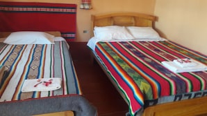 Dos camas individuales con mantas y almohadas de colores, un cabecero de madera y una pared roja con un tejido colgante.