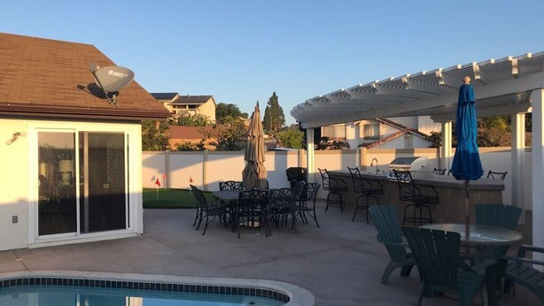 Un jardin avec une piscine, des meubles de patio et un espace barbecue couvert.