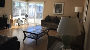 Un salon comprenant un canapé, une table basse, une lampe, un téléviseur et une fenêtre avec des stores.