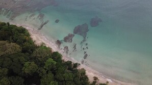 Vista aérea de una playa con aguas turquesas cristalinas, afloramientos rocosos y zonas boscosas densas.