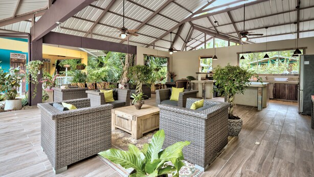 Un espacio interior amplio con mobiliario de mimbre, plantas en macetas y una zona de cocina.