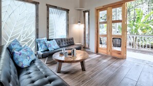 Una sala de estar moderna con un sofá de cuero, una mesa de centro redonda de madera y ventanas grandes con diseños geométricos.