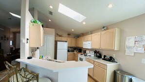 Cocina moderna con una isla central, armarios de madera, microondas y un cubo de basura de acero inoxidable.