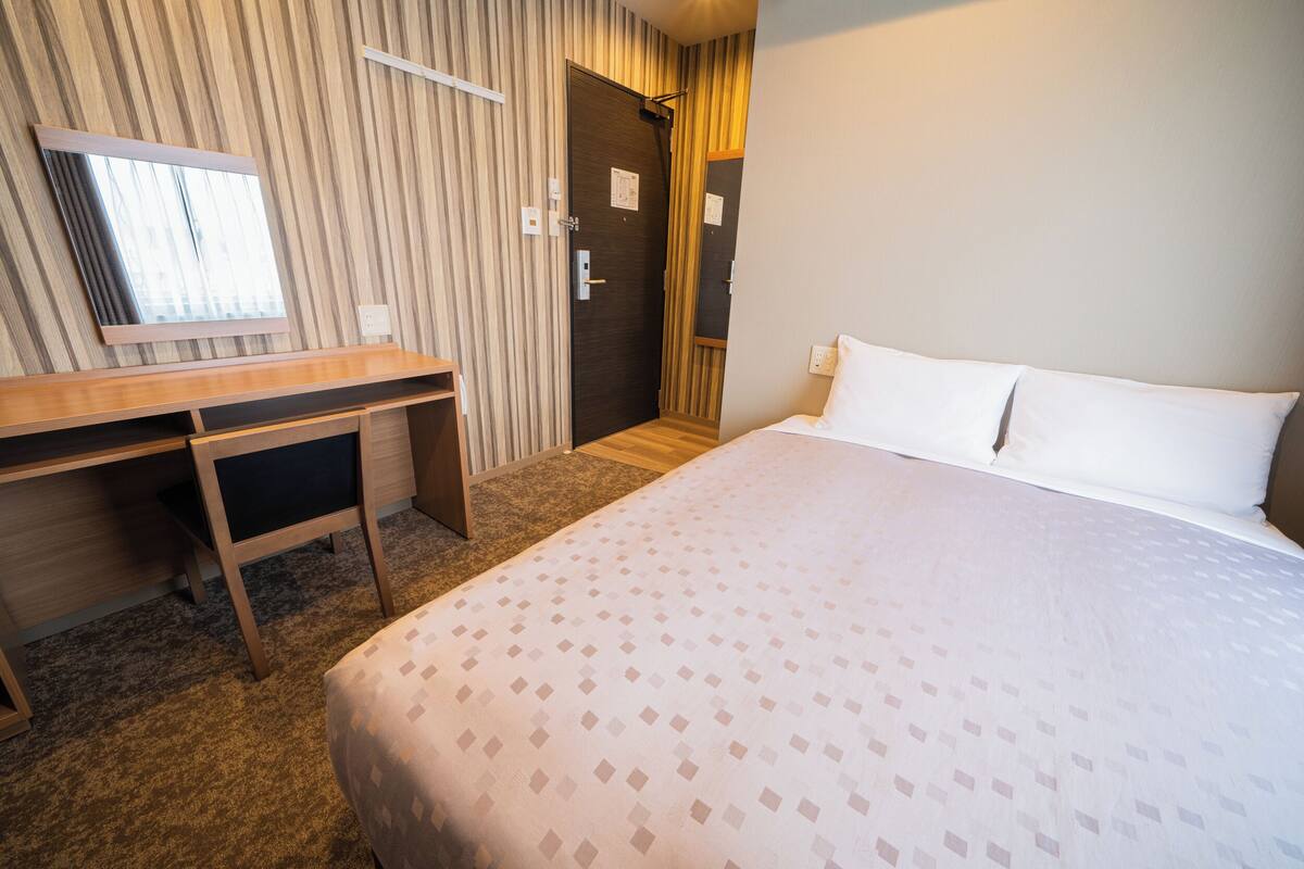 Una habitación de hotel con cama, escritorio, silla, espejo y puerta.
