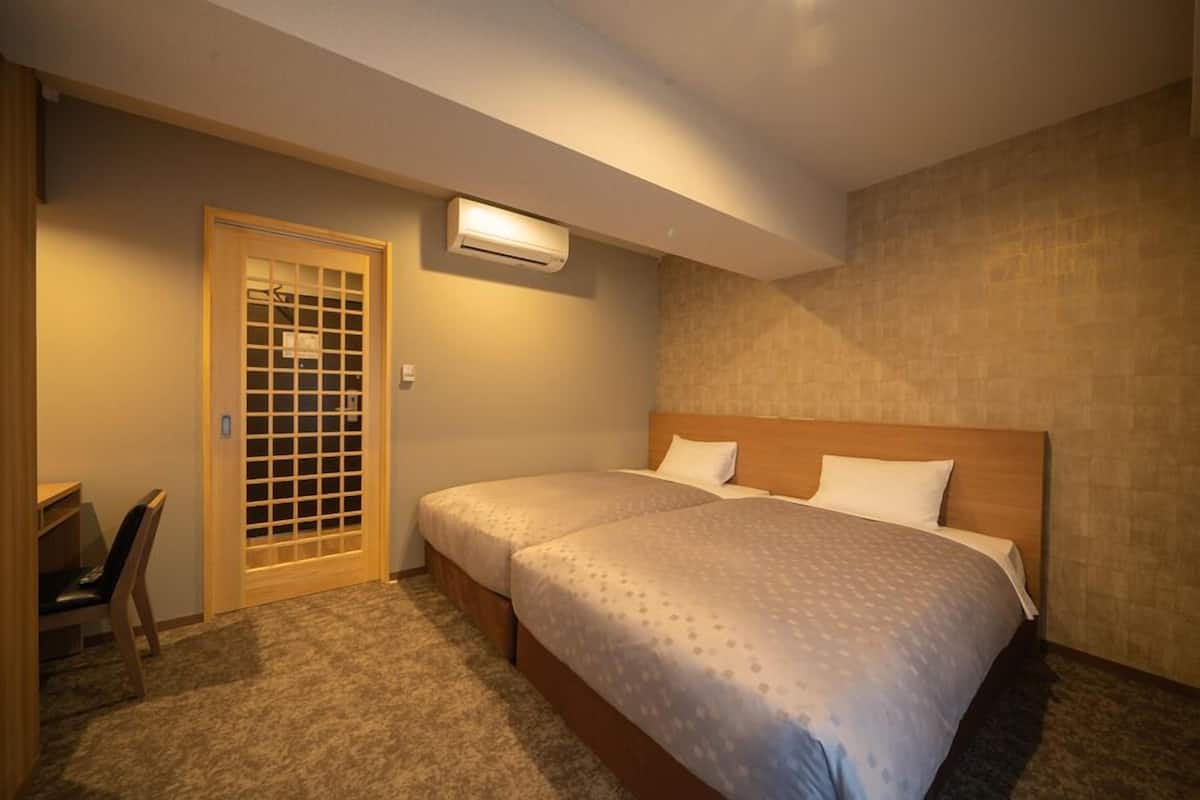 Quarto de hotel com cama, escrivaninha, cadeira, guarda-roupa e ar condicionado.