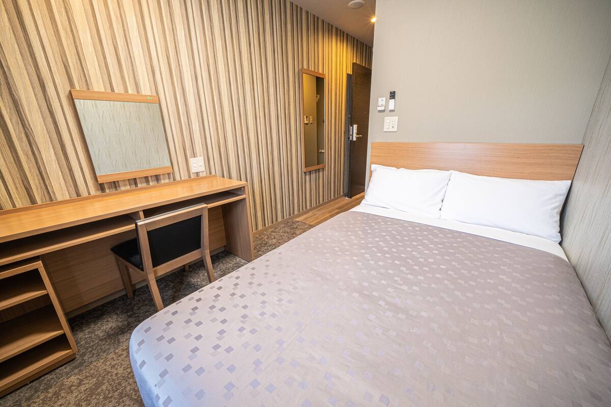 Habitación de hotel con una cama, un escritorio con espejo y una puerta que da al baño.