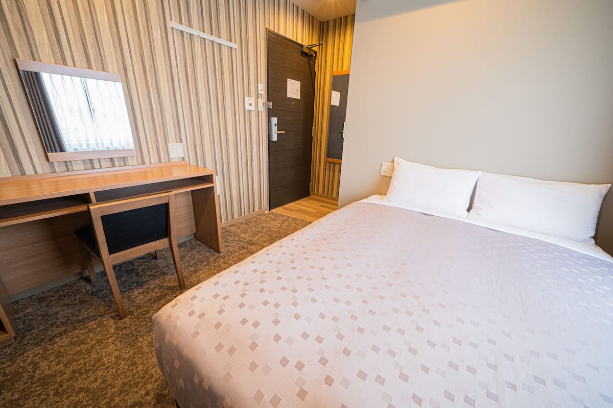 Una habitación de hotel con una cama, un escritorio, una silla, un espejo y una puerta.