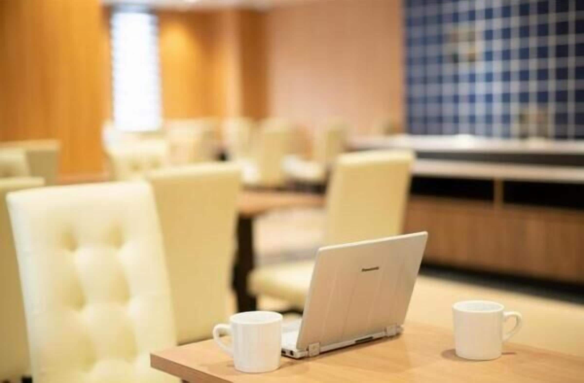 A modern hotel room with a wooden table, a laptop, and two white mugs.