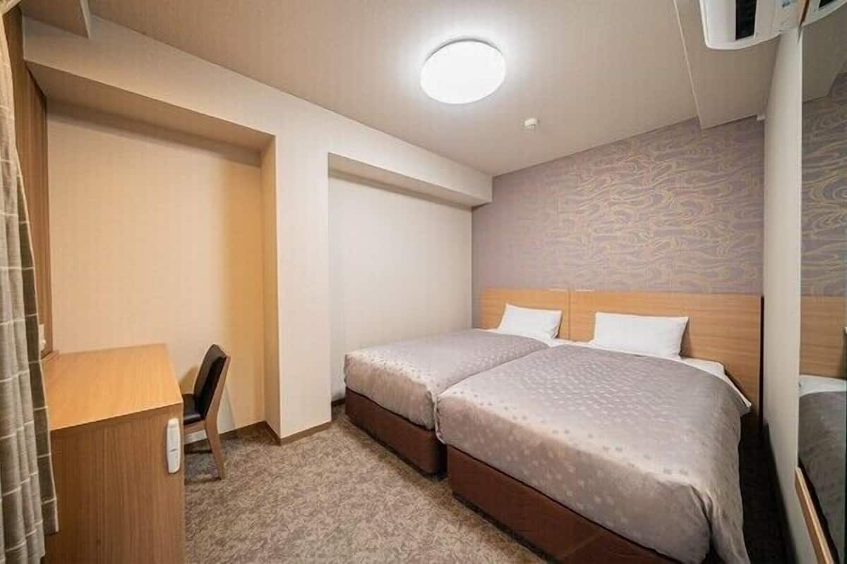Quarto de hotel com duas camas, uma escrivaninha e uma cadeira.